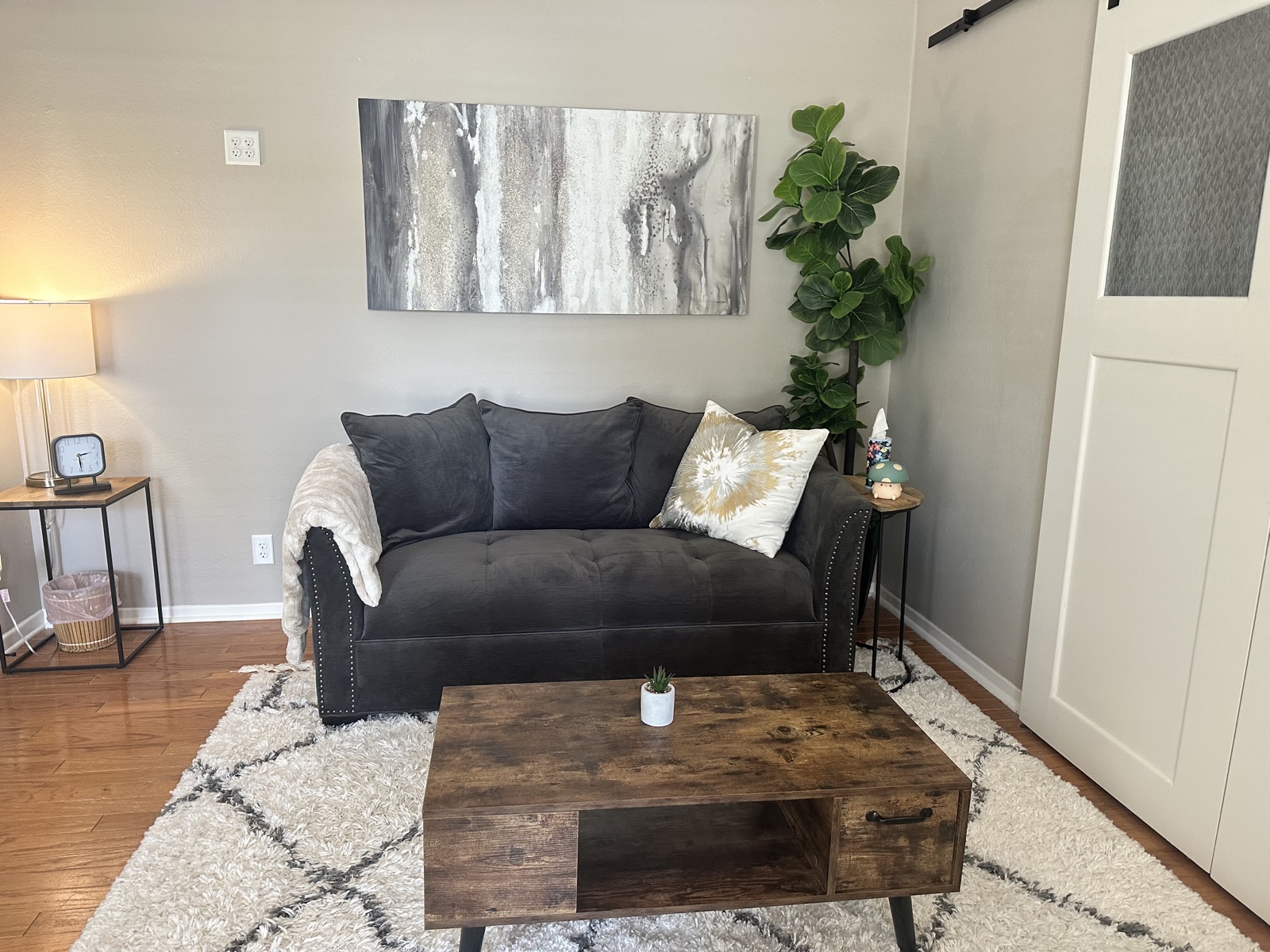 A calm, softly lit lounge at the Katy office, with a dark velvet couch, a warm throw blanket, and a leafy plant in the corner.